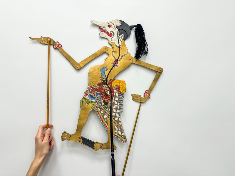 Marioneta con la figura de un hombre con cola de caballo donde se puede ver la mano de una persona operando uno de sus palitos