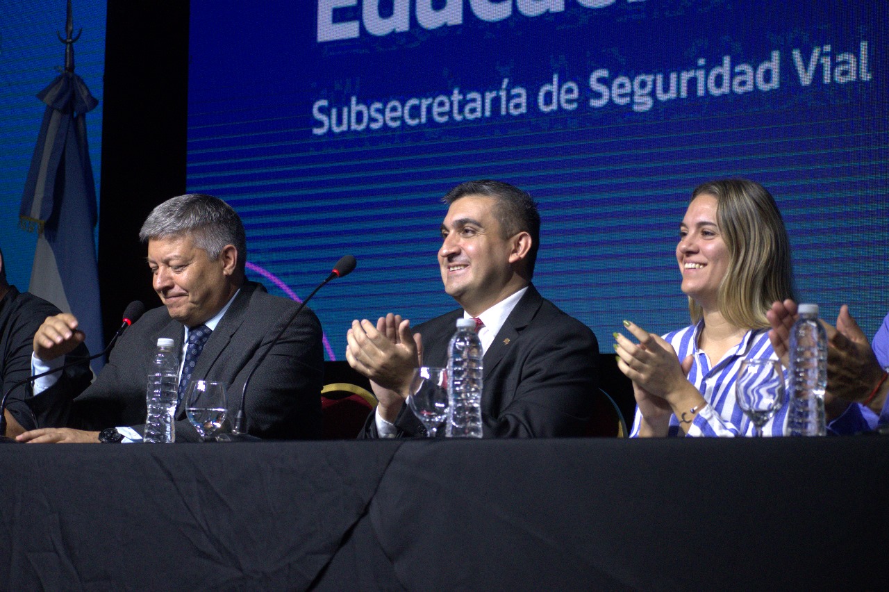 Jornada de capacitación, tres de los oradores de la jornada sentados frente a mesas con mantelería y micrófonos, detrás una pantalla con el logo institucional de la Secretaría Provincial de Seguridad Vial