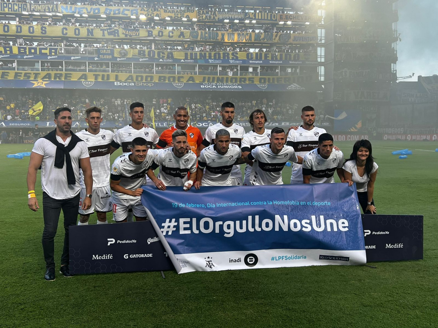 La titular del INADI, Greta Pena, y el plantel de Gimnasia posan con una bandera con la frase: #ElOrgulloNosUne.