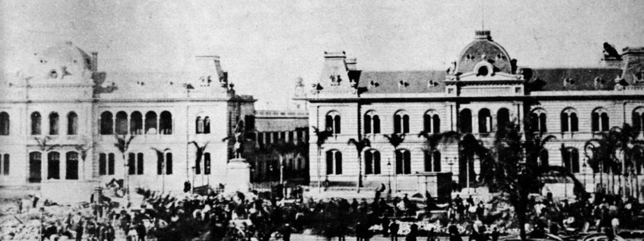 La imagen muestra una fotografía en blanco y negro de un edificio antiguo de estilo clásico. El edificio tiene varios pisos y está adornado con ventanas de arco de medio punto. 