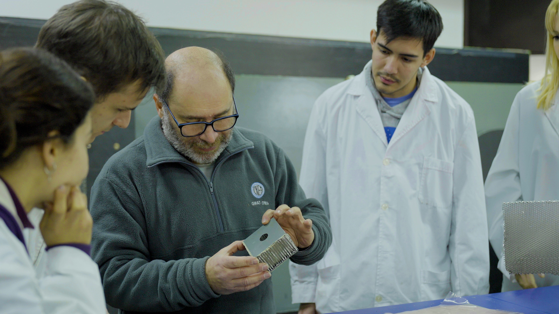 Profesor explicando a alumnos con una porción de material usado en paneles solares.