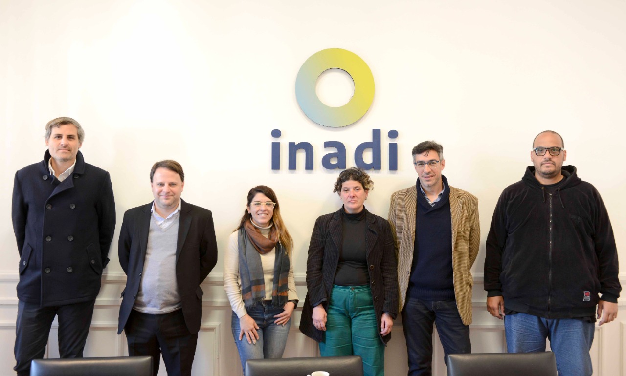 Funcionarios del INADI y el INCAA posan para la foto junto al logo INADI de la sala de reuniones