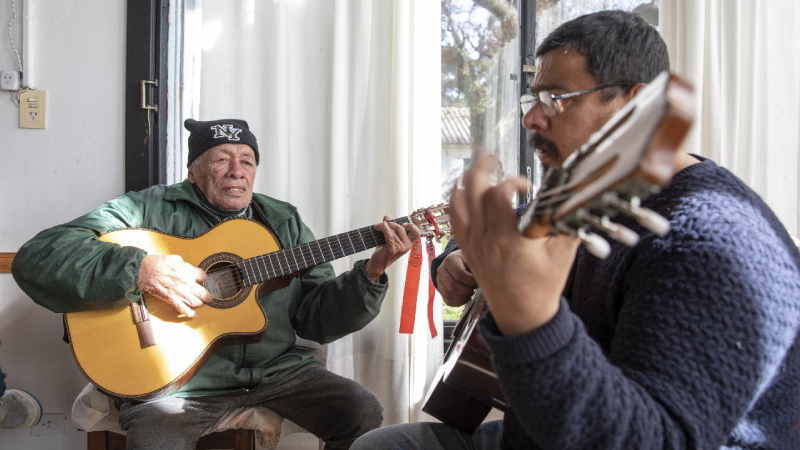 Joven y adultos mayor tocando la guitarra juntos.