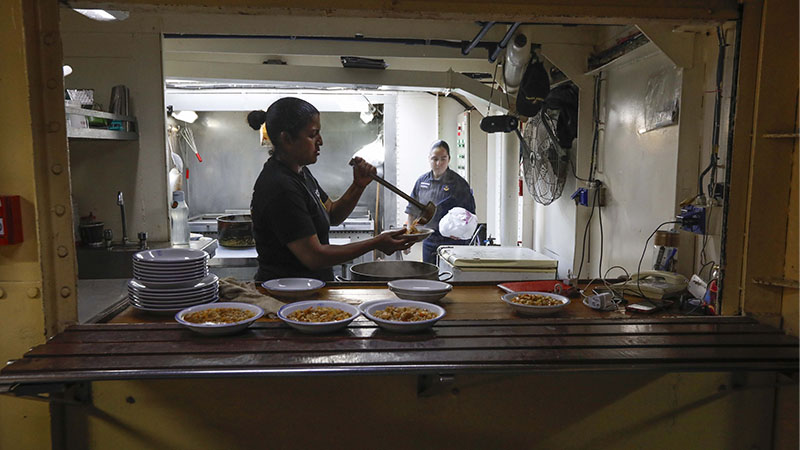 Una cocinera de las fuerzas armadas está sirviendo la comida a la tropulación a bordo.