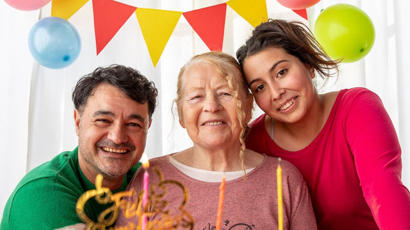 Adulta mayor junto a dos personas festejando su cumpleaños.