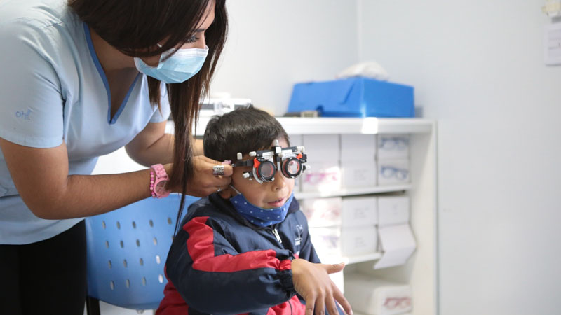 Una oculista le está colocando un instrumento de medición visual a un chico.