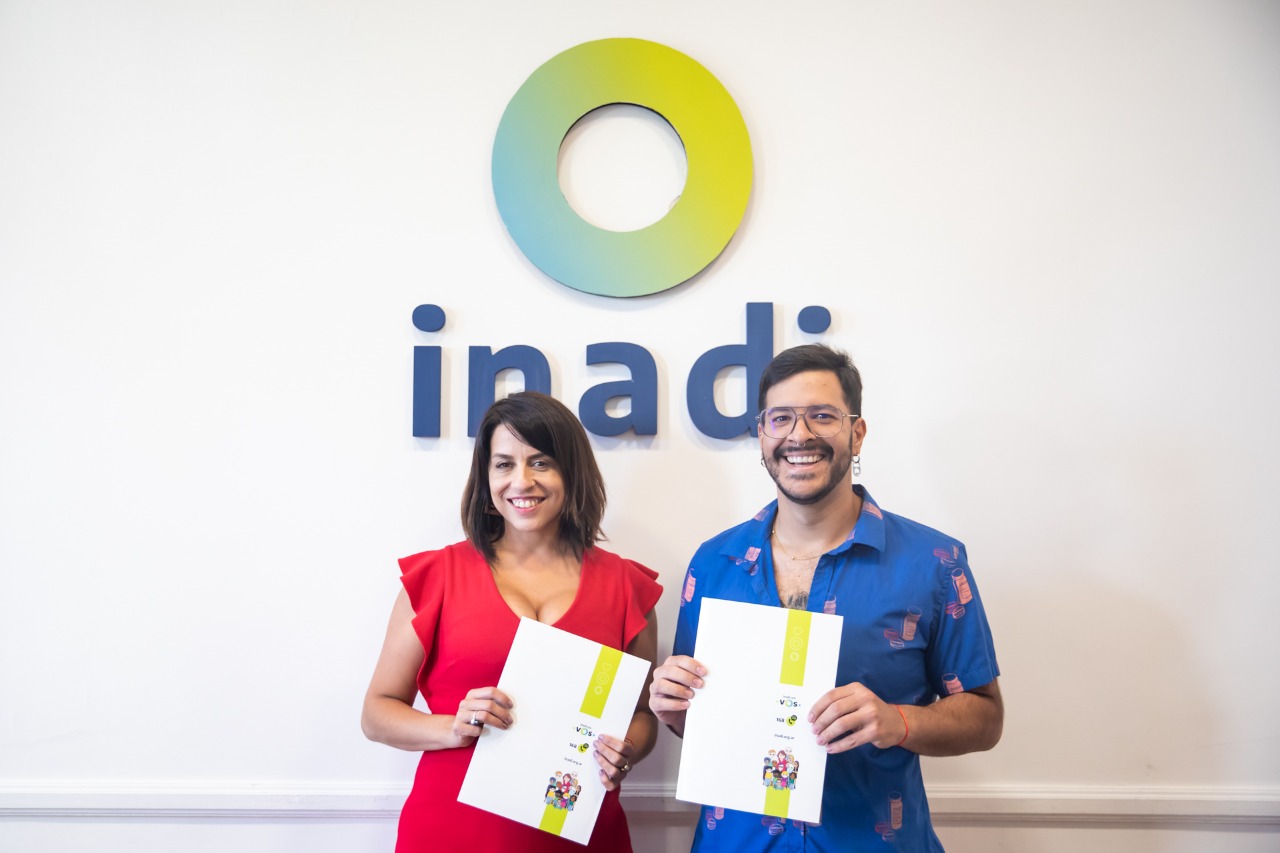 Donda y Villalba posan con los convenios en la mano bajo el logo INADI en la sala de reuniones del organismo.